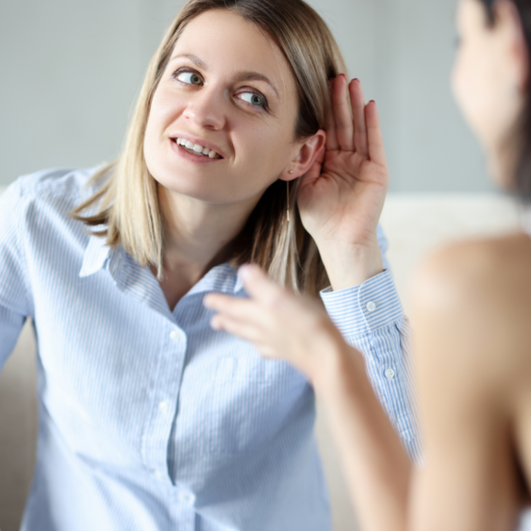 Young woman holding her ear while talking to a friend, indicating she may be having difficulty hearing or is trying to listen closely.