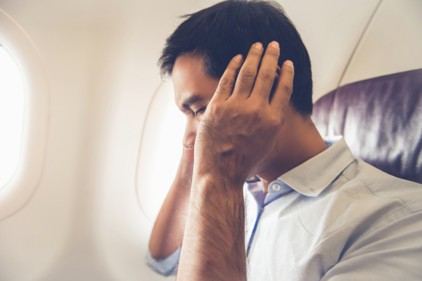 A man on a plane, covering his ears with his hands.
