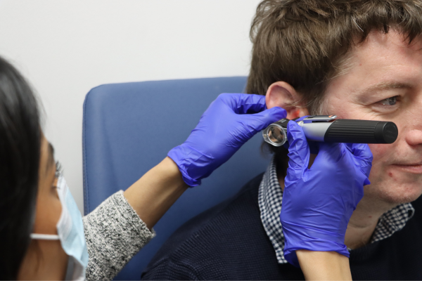 Audiologist examining a patient's ear with an otoscope, focusing on the ear canal and eardrum.