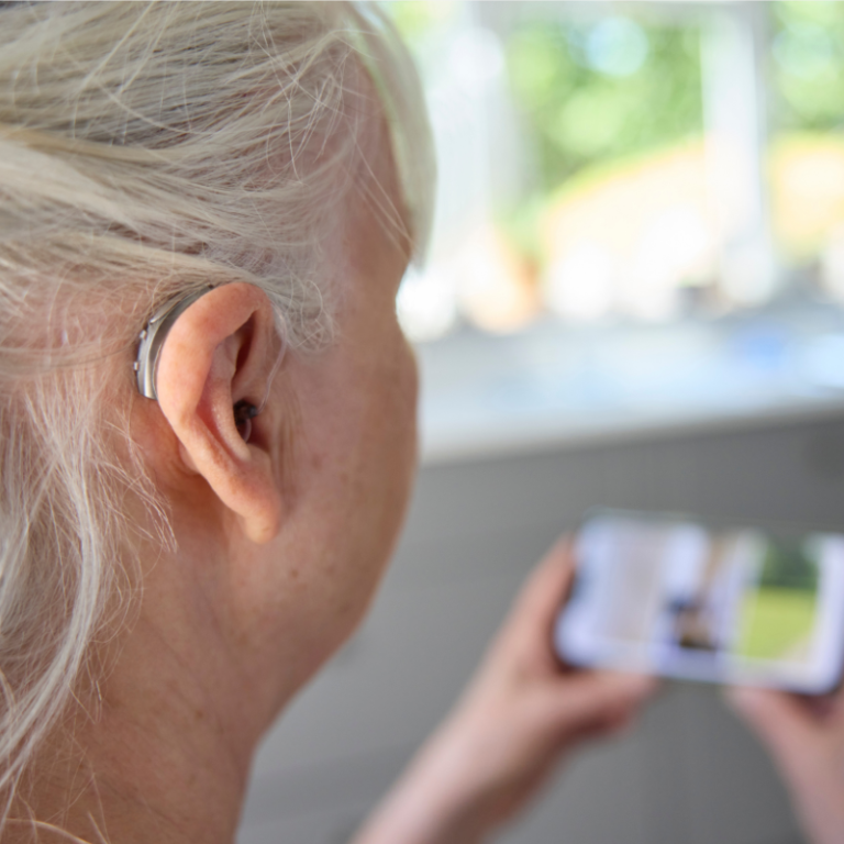 Close-up of a senior woman wearing a BTE hearing aid, enjoying a film streamed from her mobile phone, highlighting modern technology in hearing assistance.