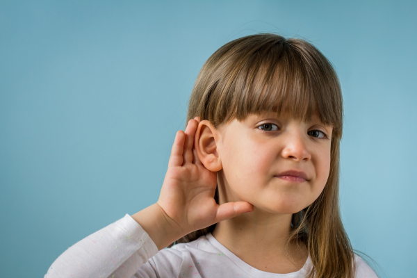 A child with a hearing impairment, standing against a blue background.