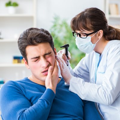 A healthcare professional inspecting a patient's ear with an otoscope while the patient appears to be experiencing discomfort.