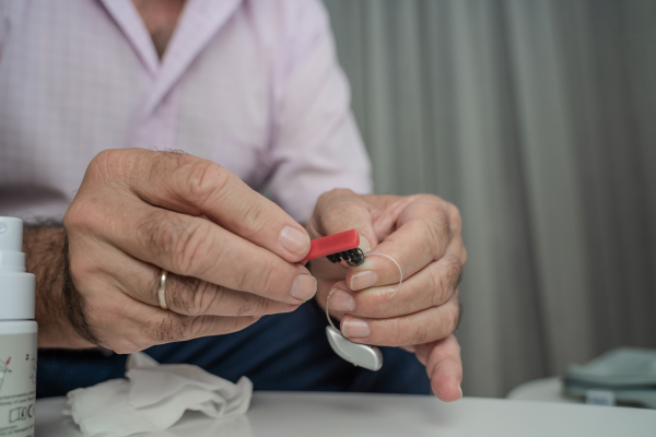 An elderly grandfather carefully cleaning his hearing aids over a table.